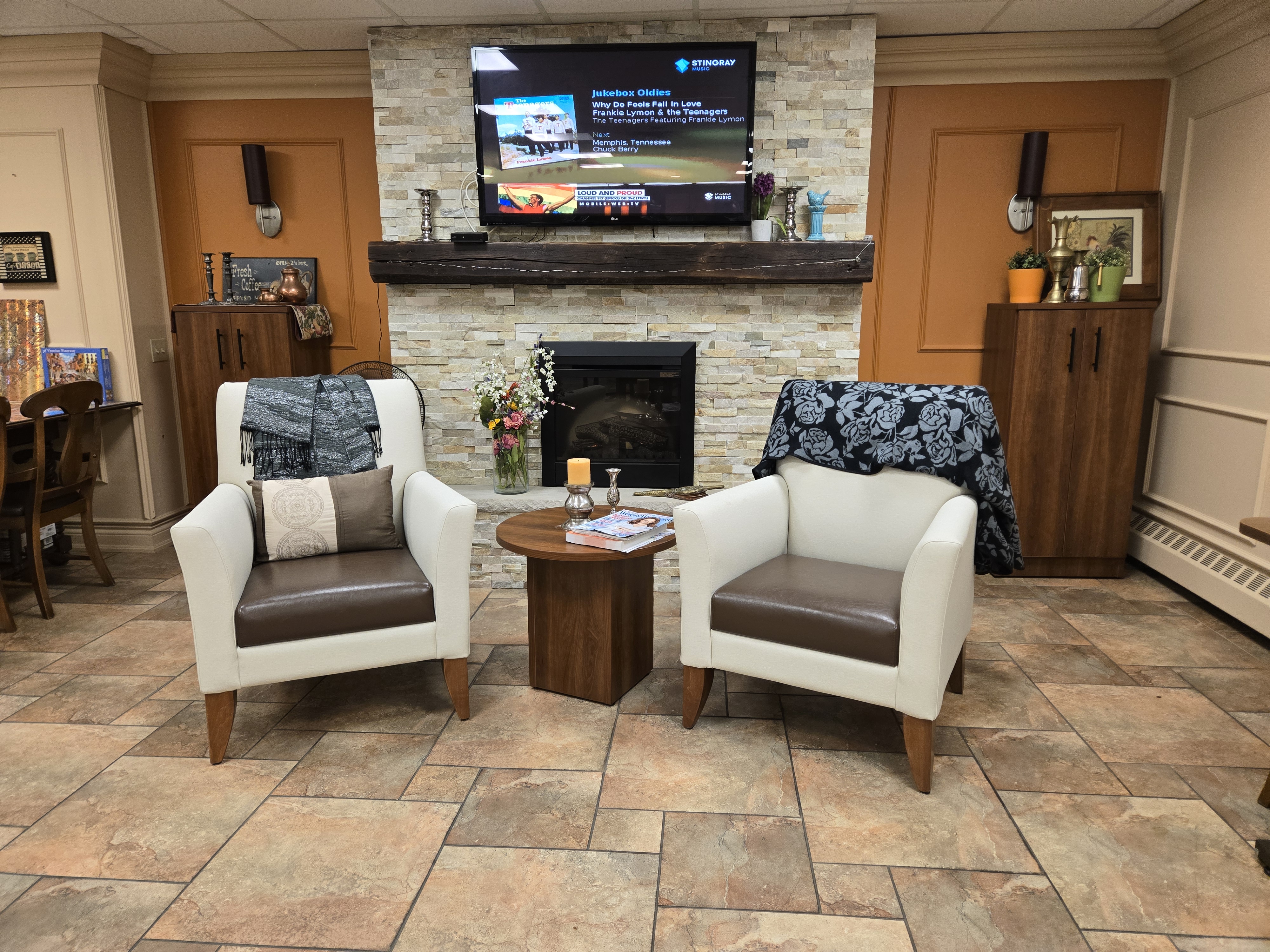 Common-area lounge with IntelliCare lounge seating and a round walnut occasional table by the fireplace